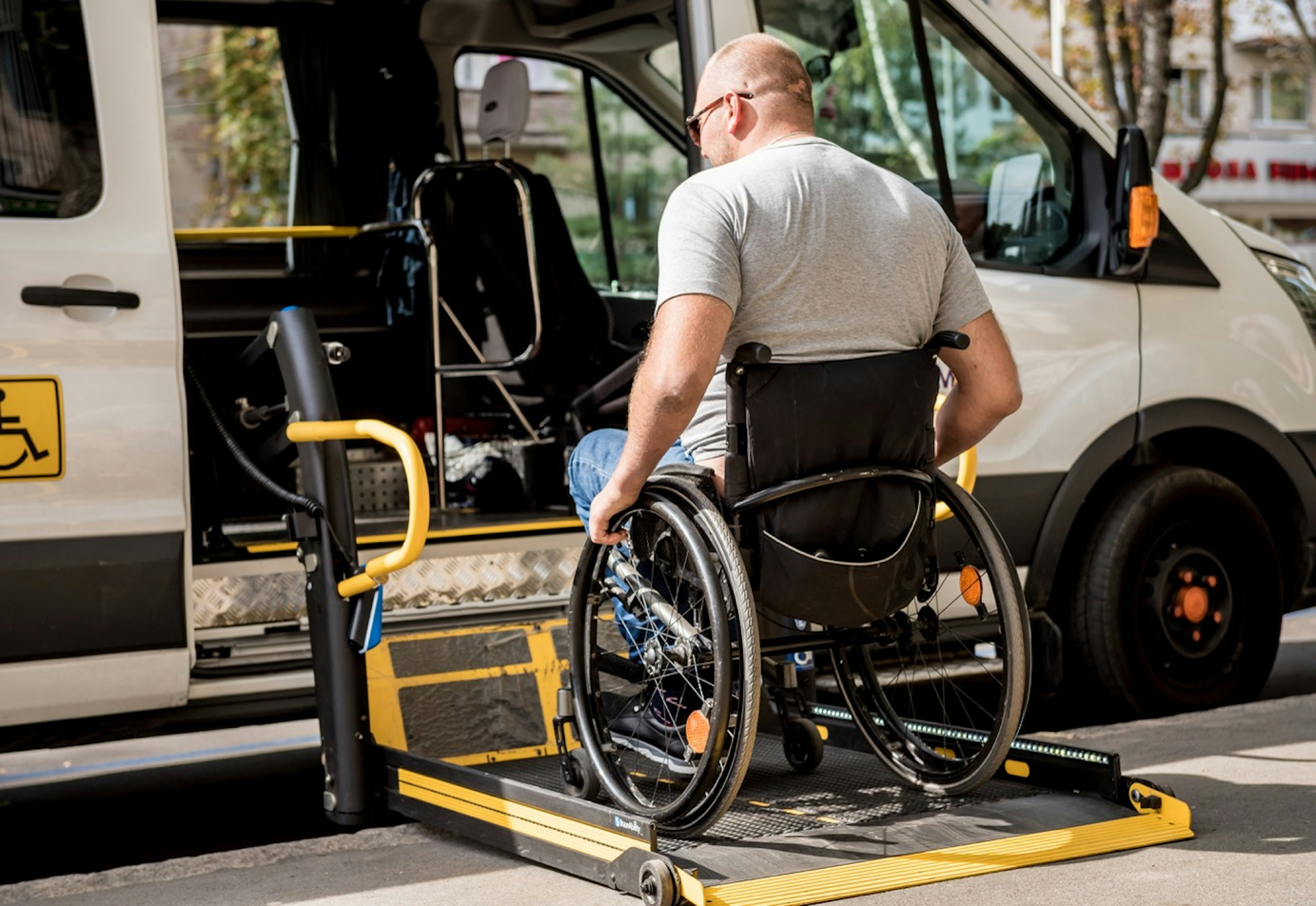 Wheelchair user positioned on a lowered platform lift entering an accessible transit van parked at the curb.