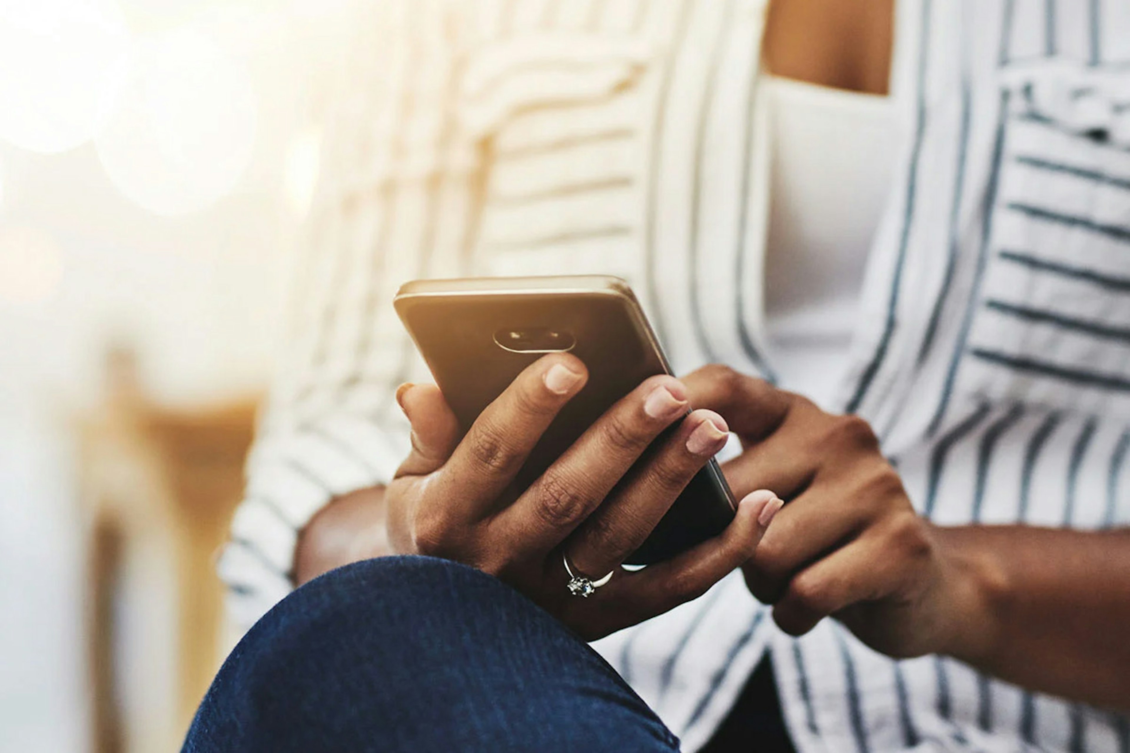 A person seated outdoors looks down at a smartphone in their hands.