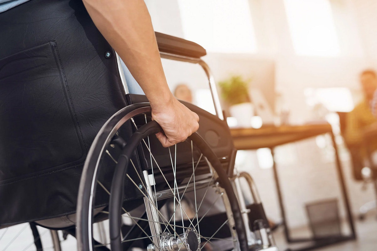 Close-up of hands gripping a wheelchair wheel inside a public building.