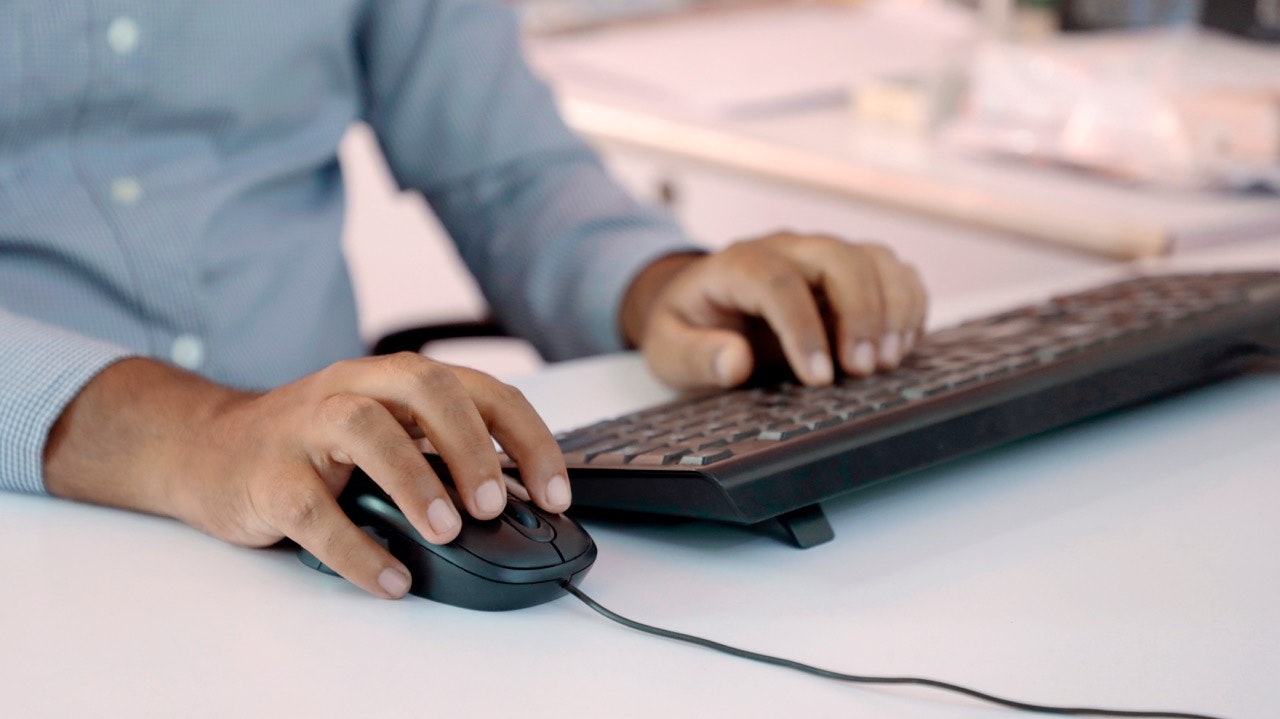 Hands using a computer mouse and keyboard at a desk, representing online or self-service work.