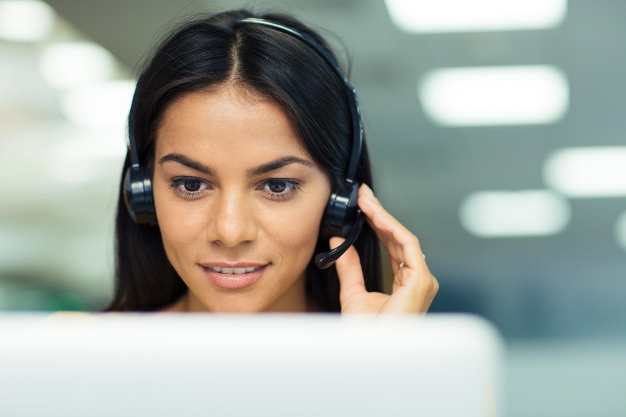 Customer support agent wearing a headset focuses on a computer screen while assisting a customer.