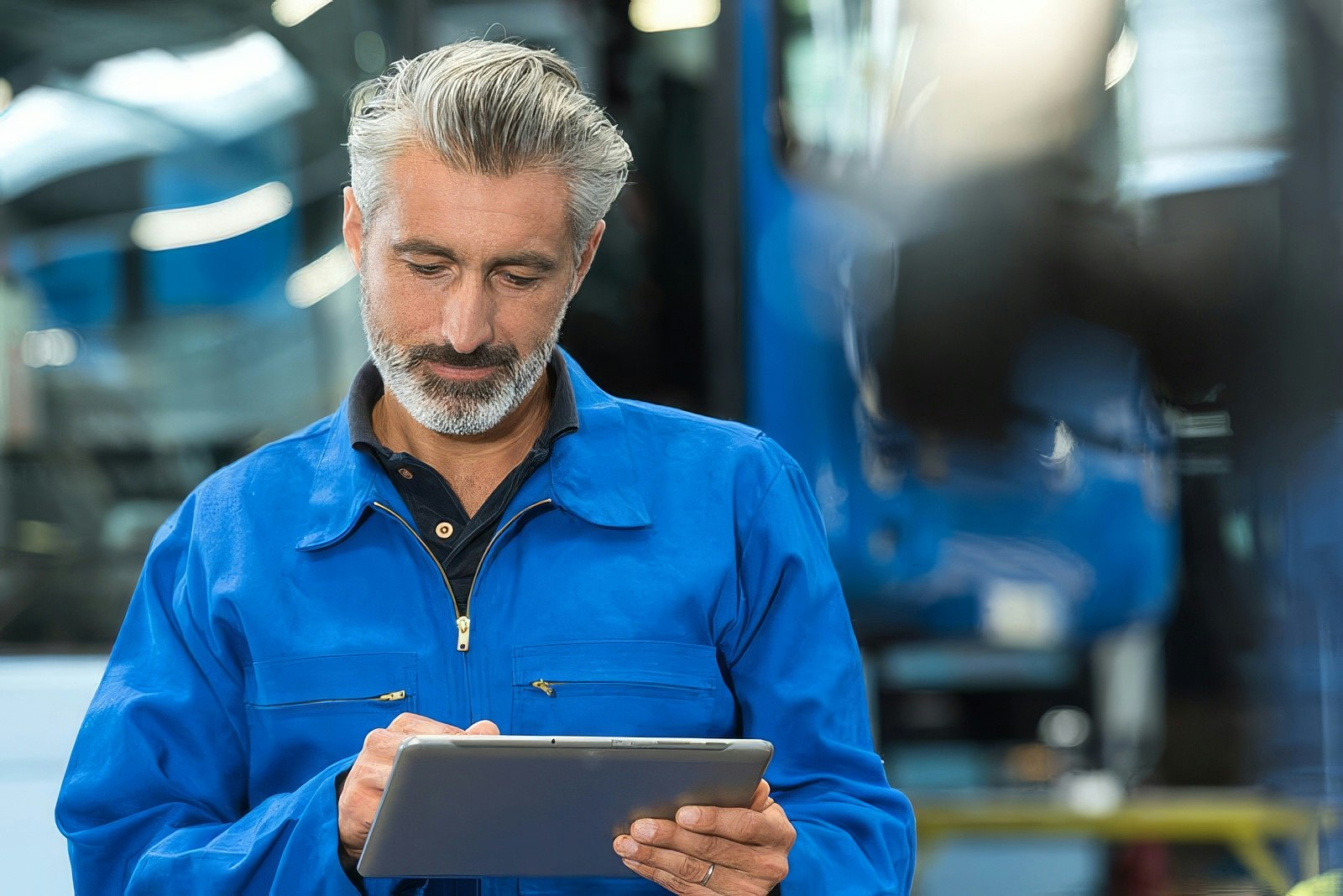 Transit maintenance worker in a blue uniform uses a tablet to complete a vehicle inspection inside a maintenance facility.