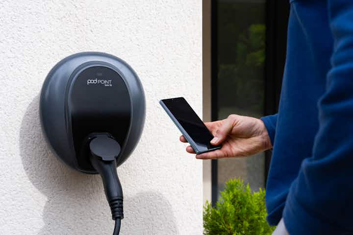 Man holding a smartphone next to a Pod Point Solo 3S charger