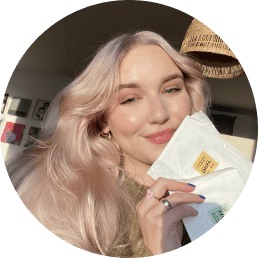 A blonde woman smiles to the camera while holding two Daye bamboo pads in super and regular sizes 