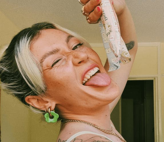 A woman has her tongue out looking at the camera holding two tampons