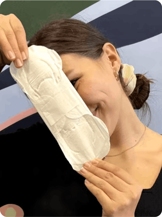 Woman smiling while holding a Daye pad in front of her face, with her hair tied back in a bun and wearing a light-colored top.