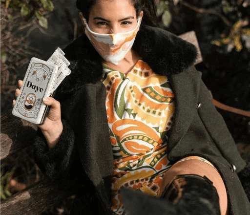Woman with face mask on her face holds an aluminium tin of organic, sustainable, pain-relieving Daye tampons for menstrual cramps 