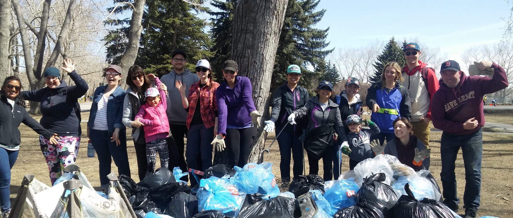 A group of people standing in front of many bags of garbage.