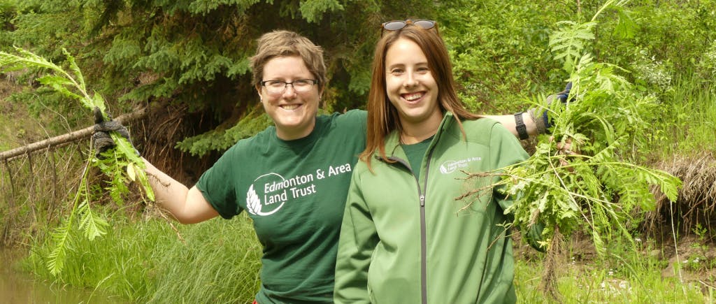 Two people holding plants and wearing Edmonton and Area Land and Trust shirts