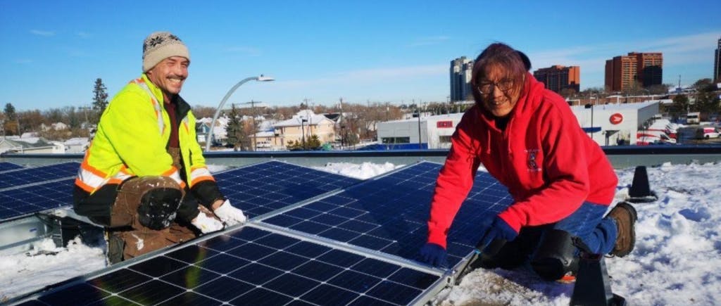 Two people crouched beside a rooftop solar array