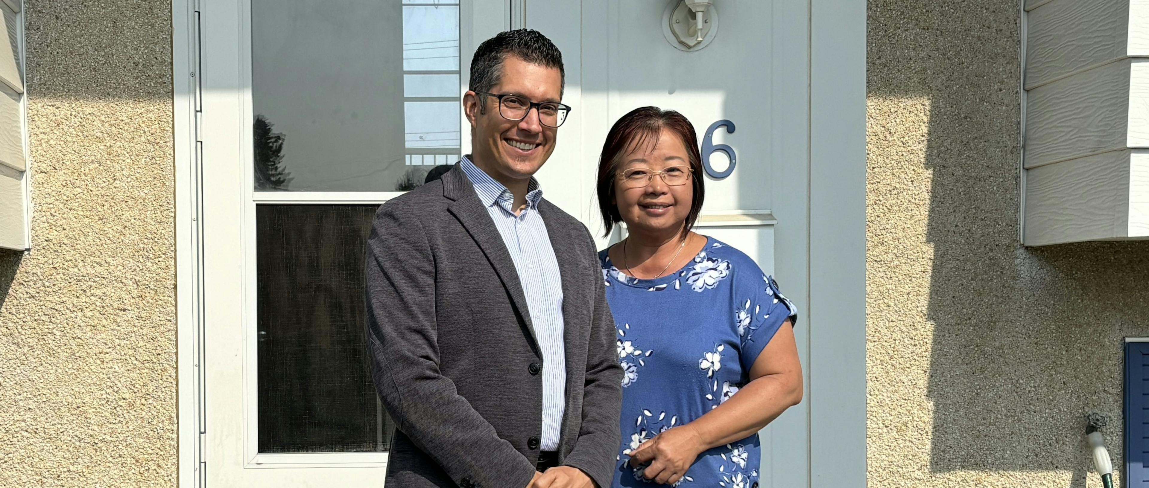 Man and woman stand next to each other in front of a house