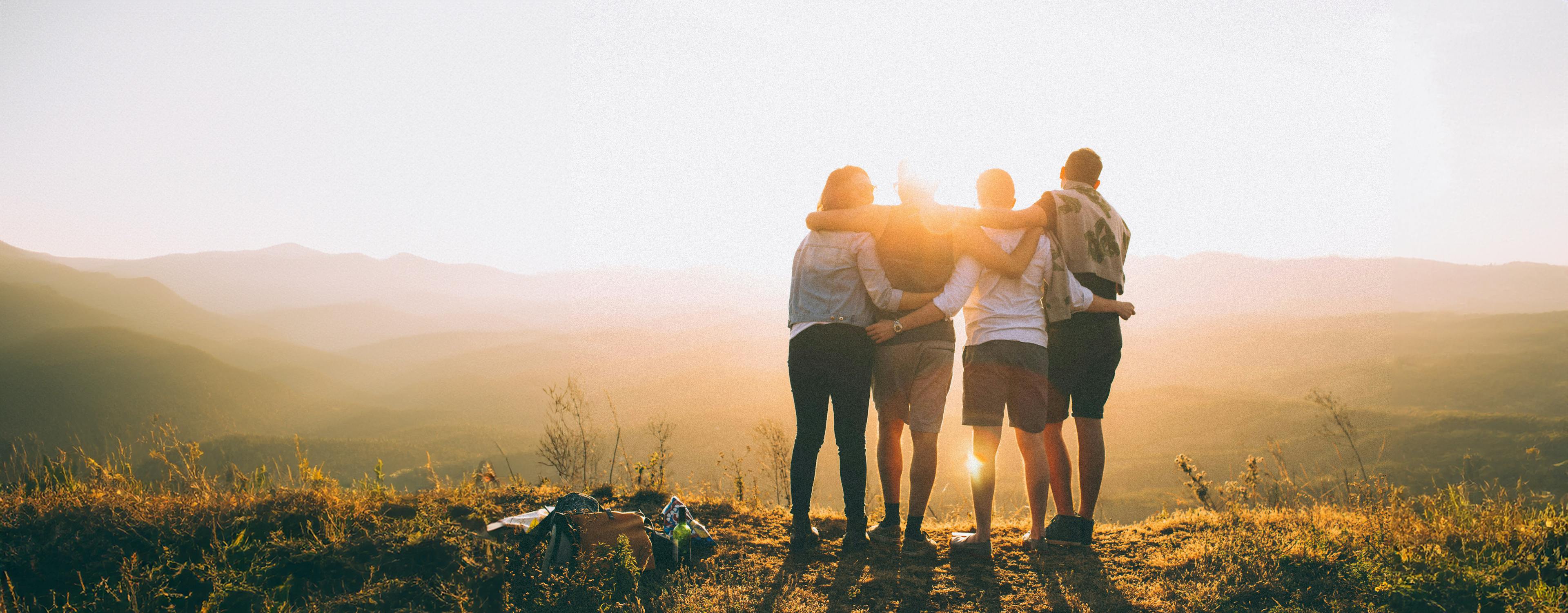 Four people with arms around each other watch a sunset