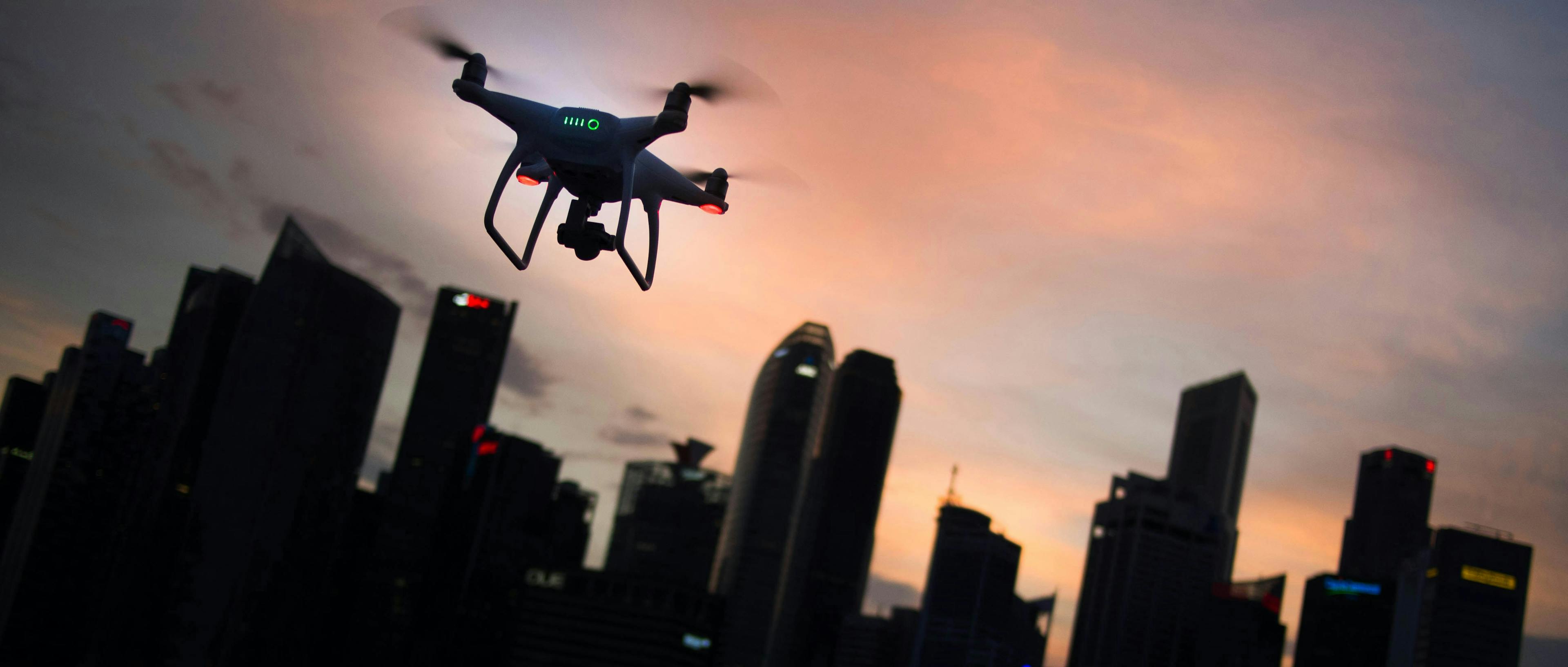 A drone flies in front of buildings at sunset