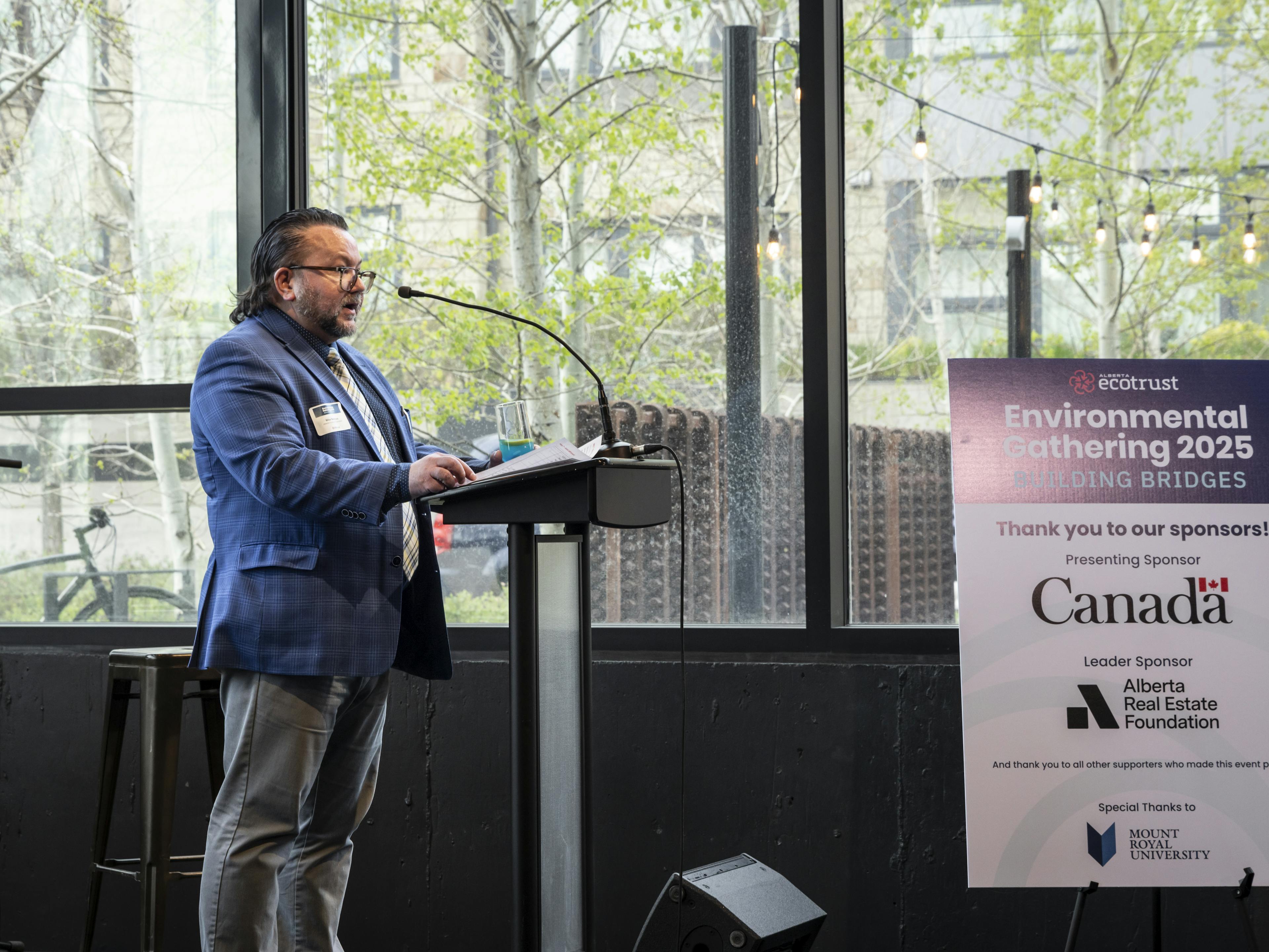 speaker on stage with sponsor sign in background