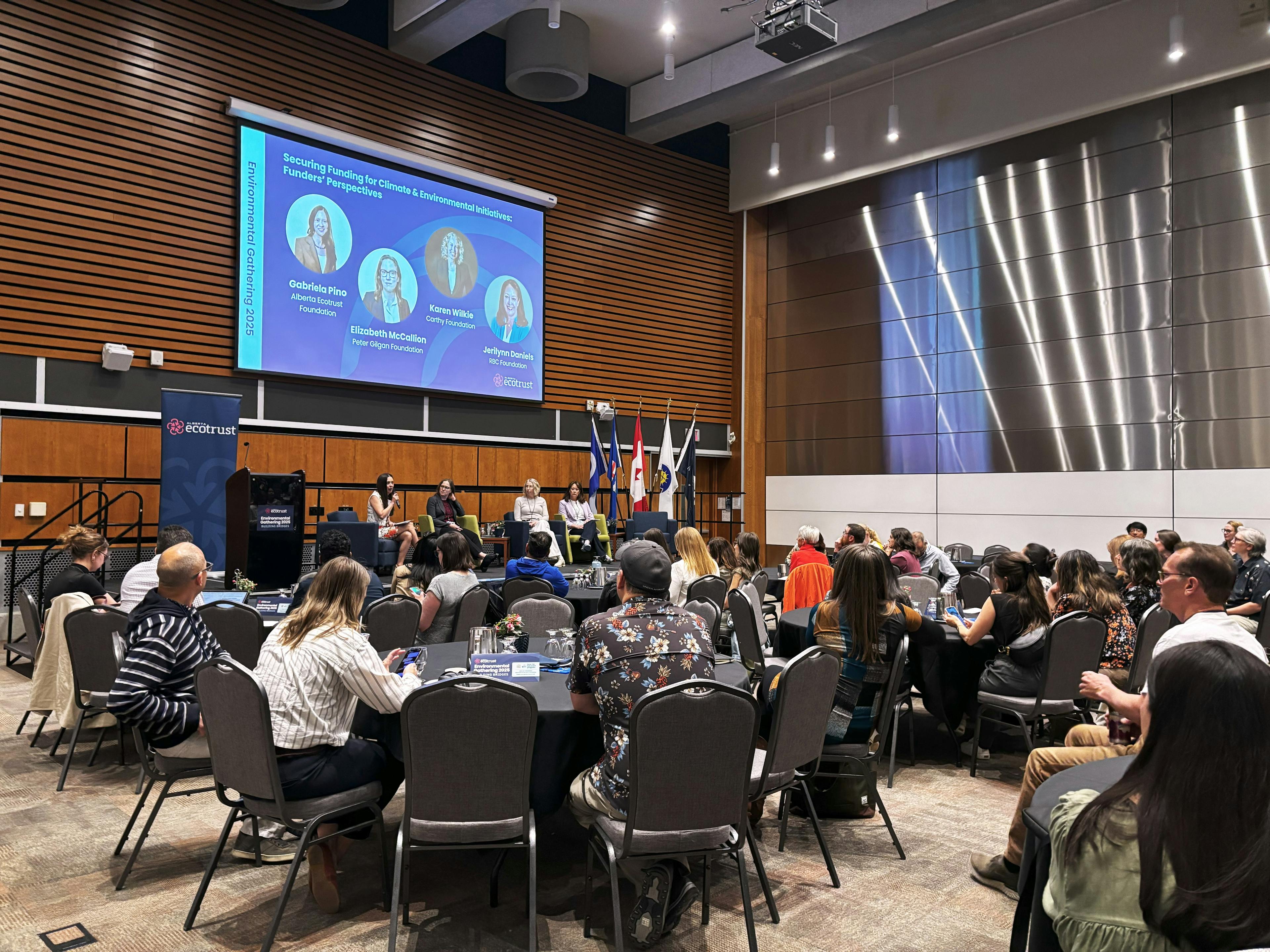 people at tables watching panel of speakers on stage