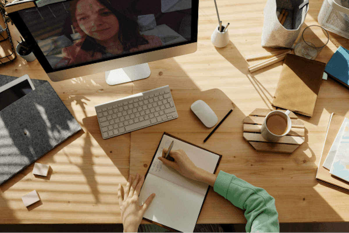 Busy desk, top view of someone writing notes in front of a monitor