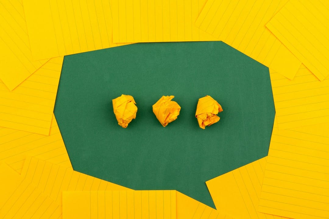 orange sheets of paper lie on a green school board and form a chat bubble with three crumpled papers