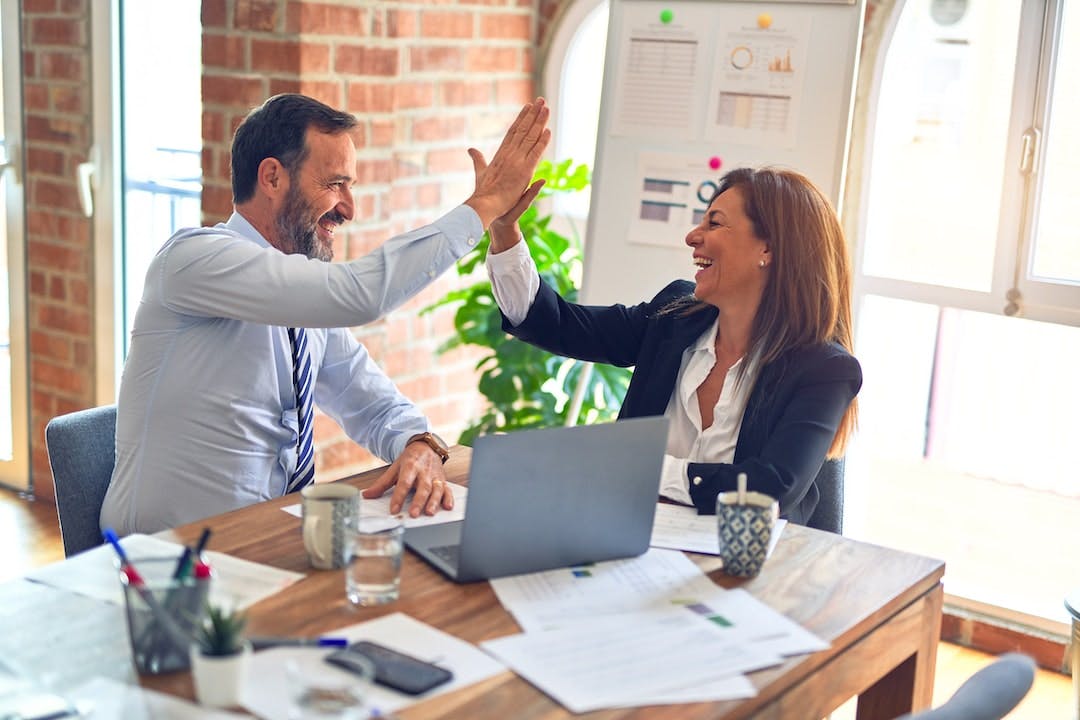 Two middle age business workers smiling happy and confident Working together with smile on face hand giving high five at the office