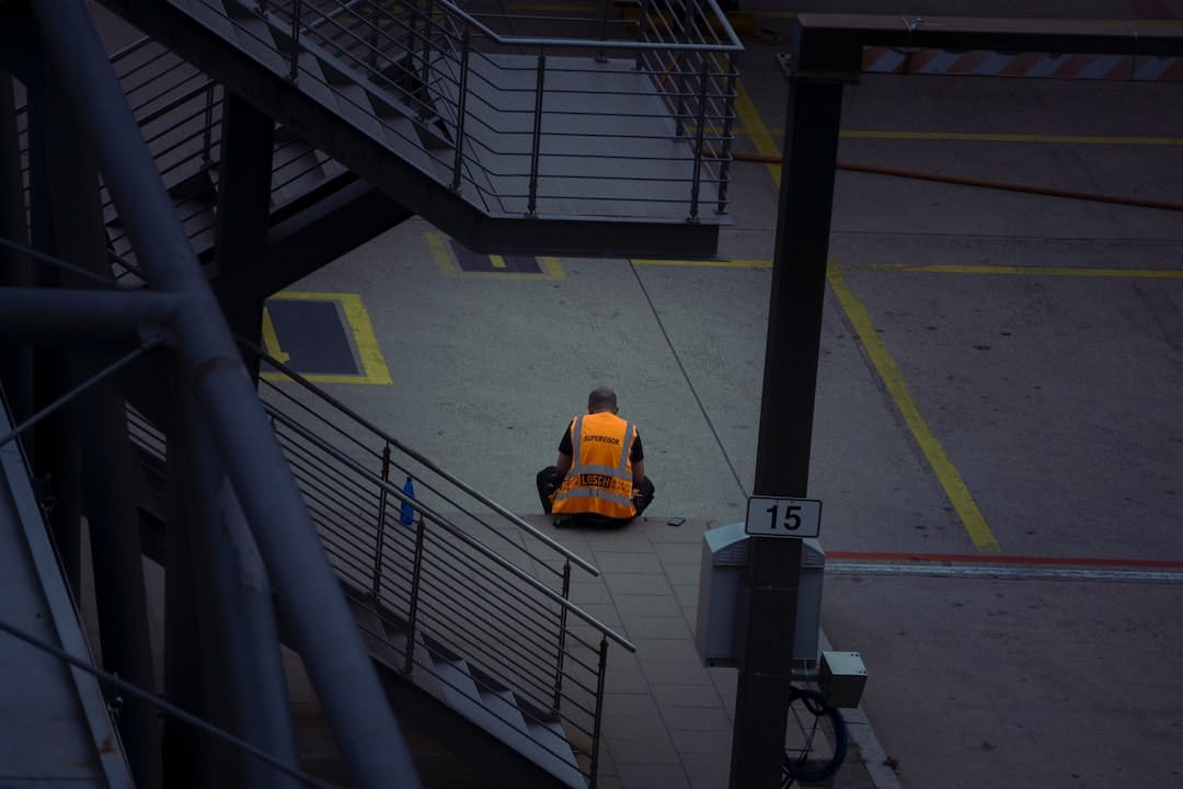 Airport supervisor wearing an orange safety vest sitting alone next to the airport runaway