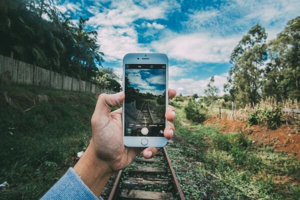 A hand holding up a phone to take a picture of a scenic view a forest