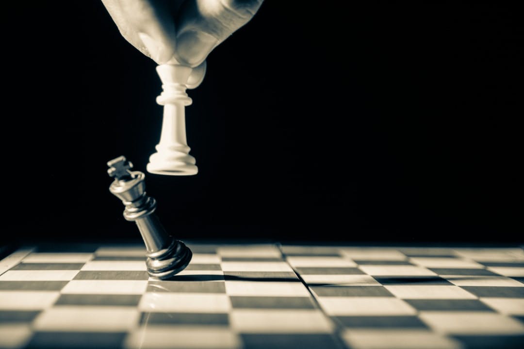 Close up of white king taking down black king Hand and fingers and chess board with vintage look
