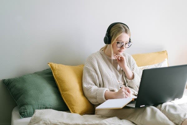 A woman with headphones on, sitting on her couch working and writing