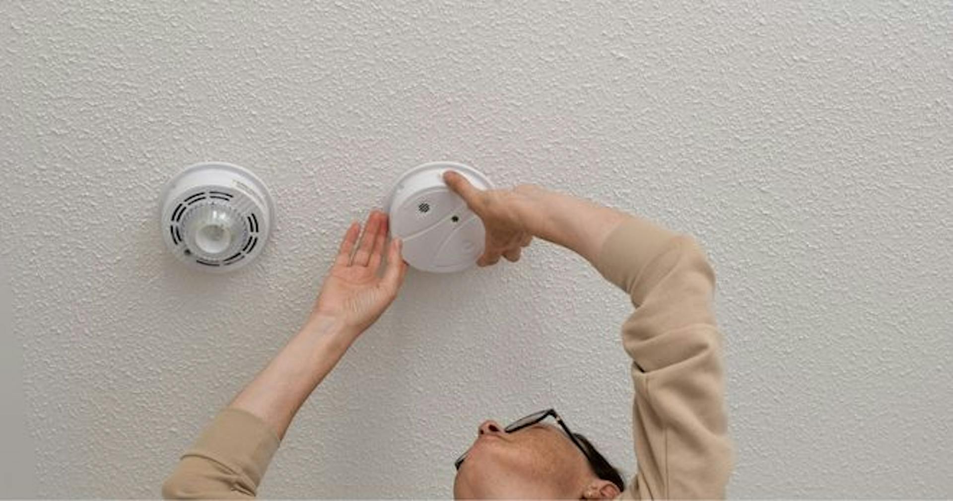 person inspecting smoke alarm and sprinkler