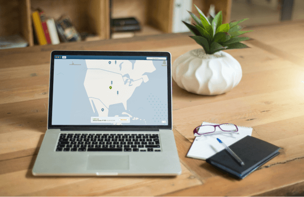 Laptop with map on screen, notebook, notepad, glasses, and glasses on the table. A plant at the background