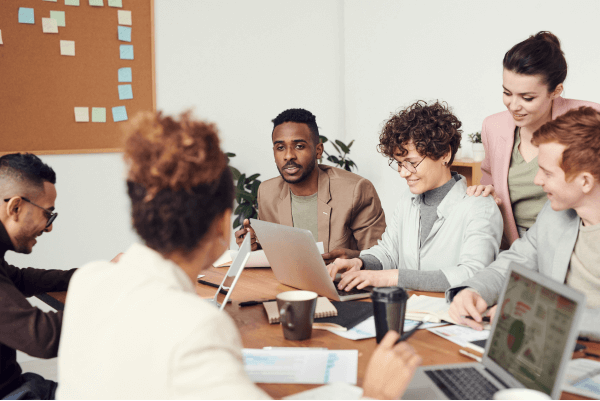 diverse people on a table talking and working on their laptops