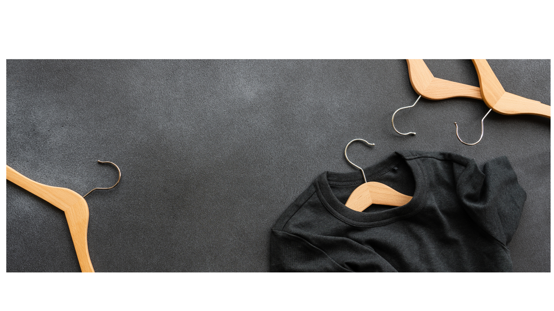 A black t-shirt on a wooden hanger lies on a dark-gray surface.