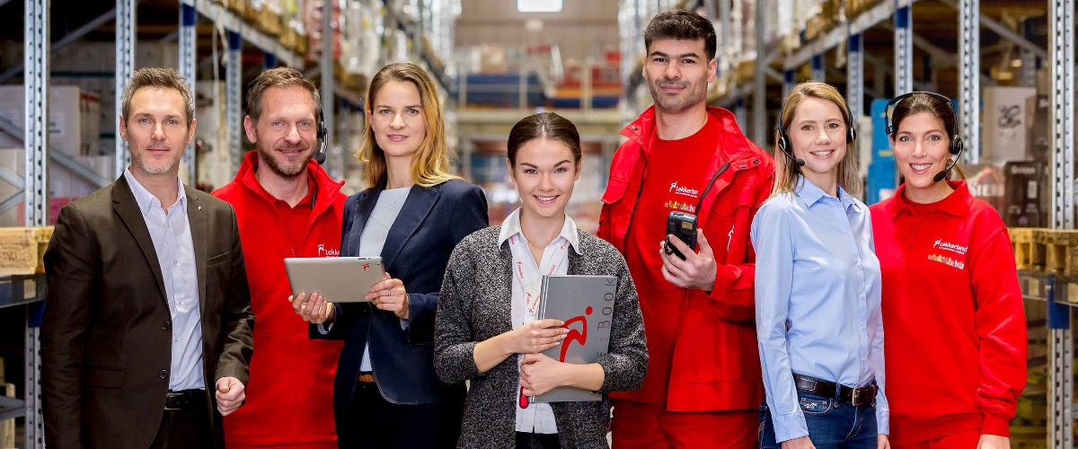 Die Mitarbeiter von Lekkerland stehen in einem Lagerhaus und lächeln in die Kamera.