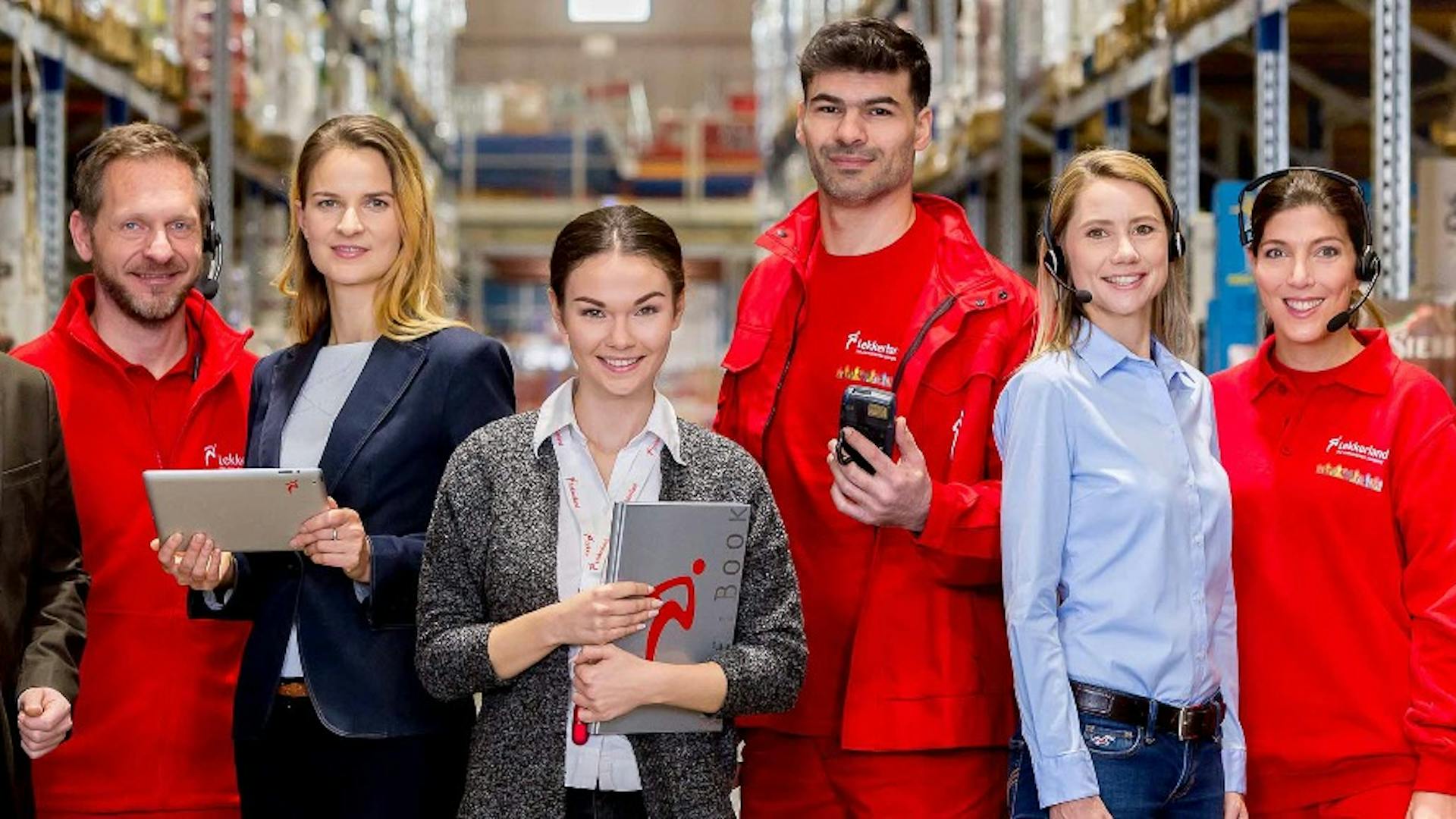 Die Mitarbeiter von Lekkerland stehen in einem Lagerhaus und lächeln in die Kamera. Die Mitarbeiter von Lekkerland stehen in einem Lagerhaus und lächeln in die Kamera.