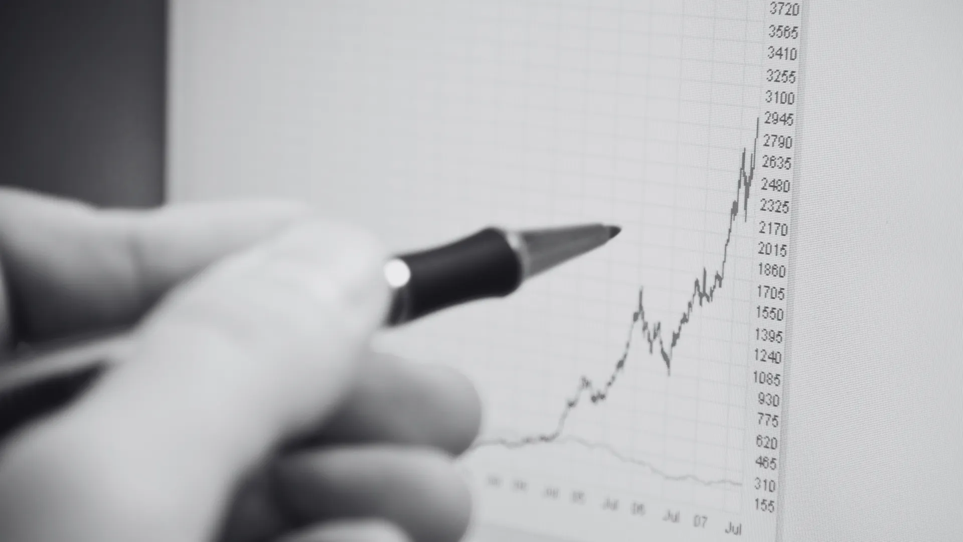 Eine Hand hält einen Stift und zeigt auf eine steil ansteigende Linie in einem Finanzdiagramm auf einem Bildschirm. Eine Hand hält einen Stift und zeigt auf eine steil ansteigende Linie in einem Finanzdiagramm auf einem Bildschirm.