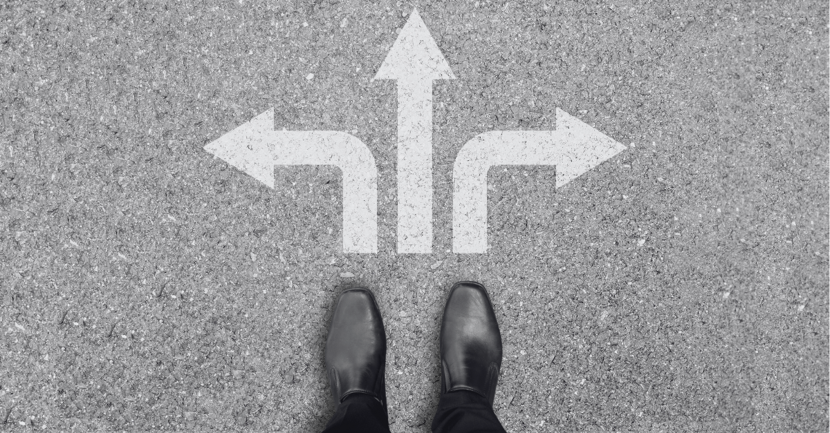 A pair of black shoes stands on a concrete surface with three large white arrows pointing left, straight, and right.