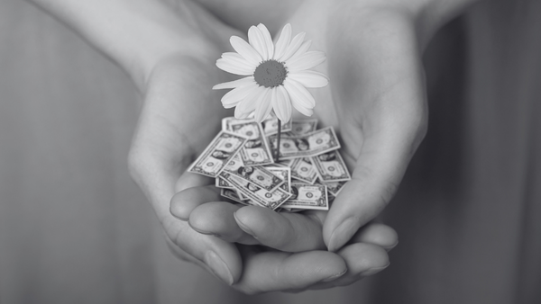 Hands holding a flower growing from a pile of dollar bills, symbolizing financial growth and stability.