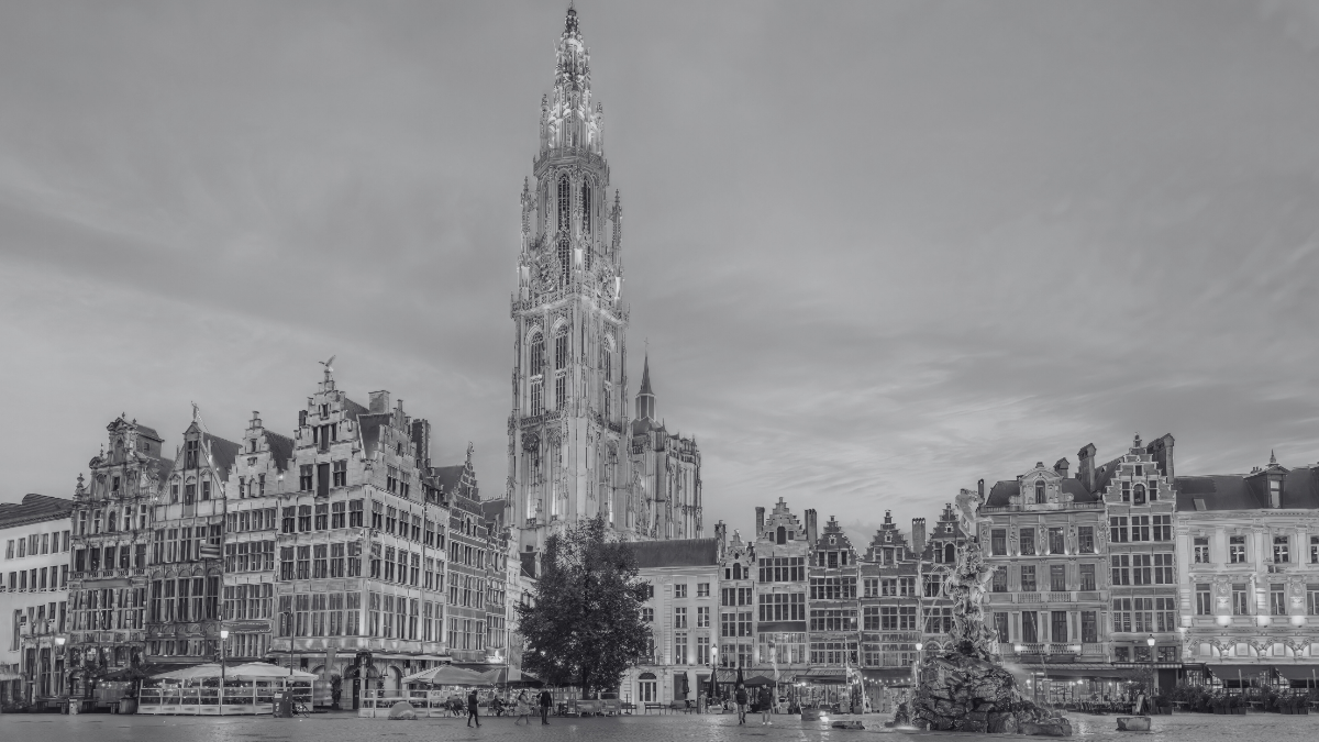Black-and-white photo of a historic square in Antwerp, Belgium, featuring the Cathedral of Our Lady, ornate guild houses, and the Brabo Fountain.