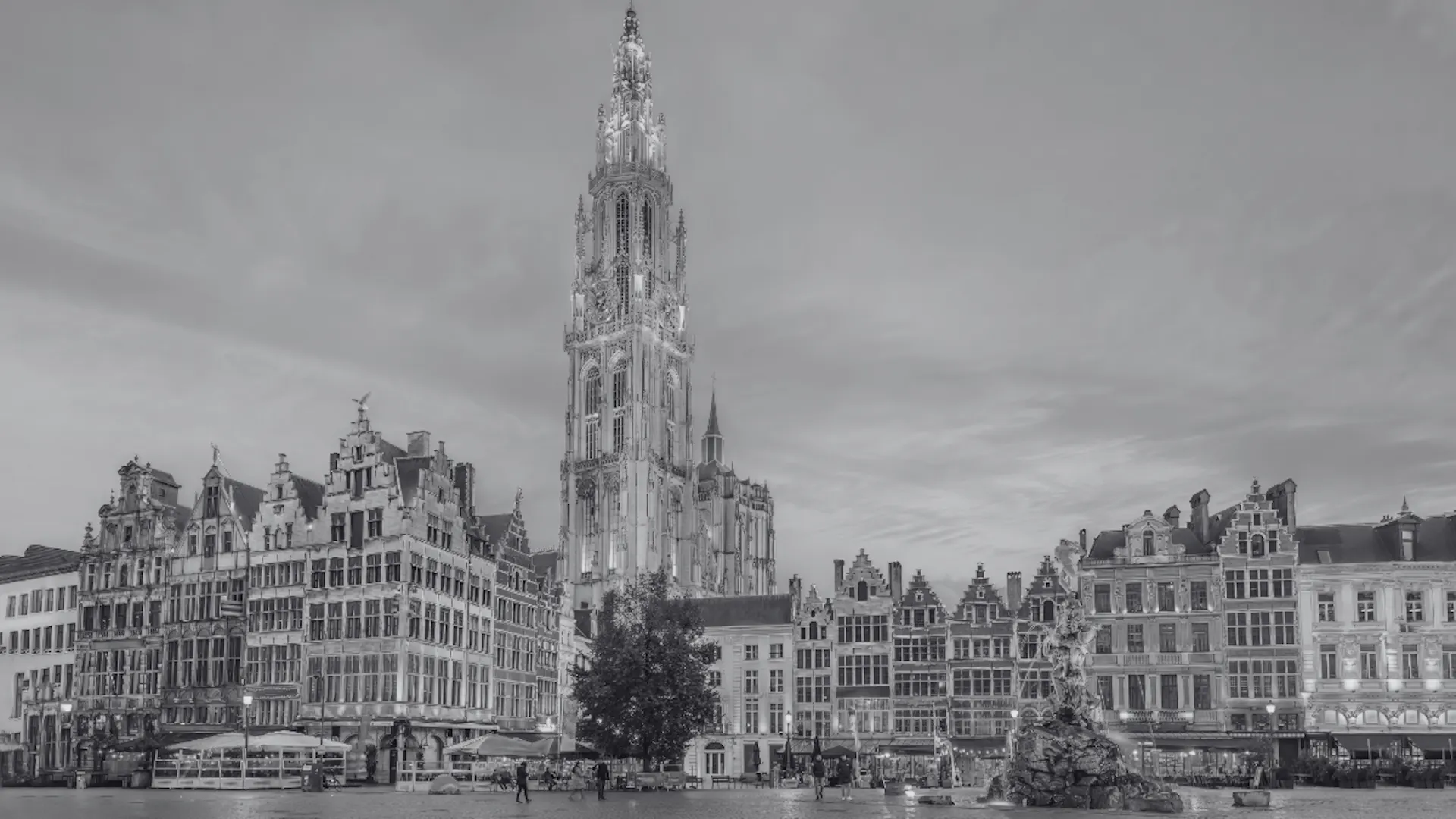 Black-and-white photo of a historic square in Antwerp, Belgium, featuring the Cathedral of Our Lady, ornate guild houses, and the Brabo Fountain. Black-and-white photo of a historic square in Antwerp, Belgium, featuring the Cathedral of Our Lady, ornate guild houses, and the Brabo Fountain.
