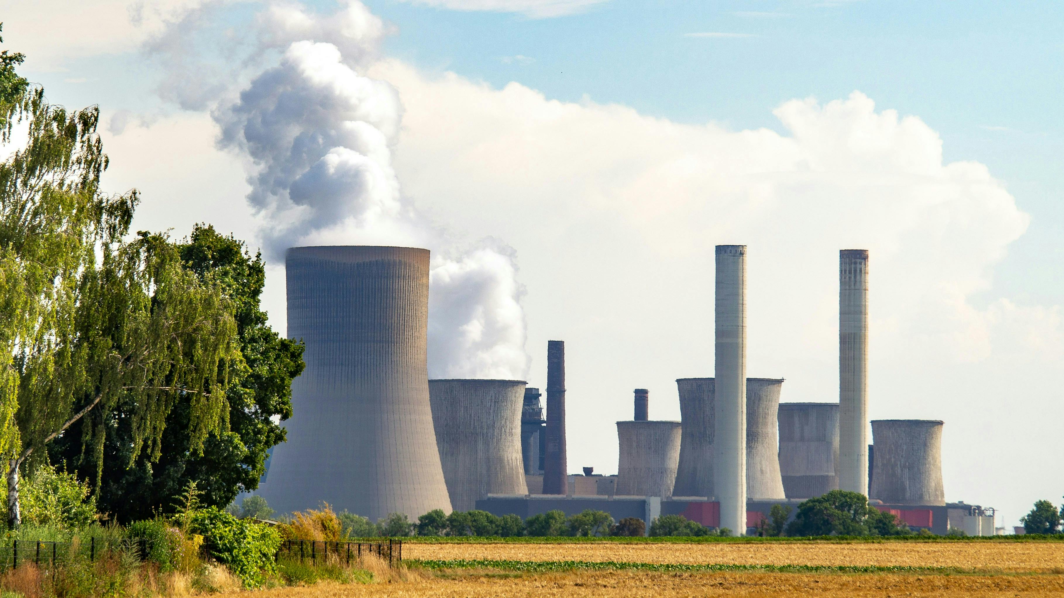 Smoke billowing from power plant towers alongside a lush field, underscoring the necessity for TNFD-guided environmental reporting.