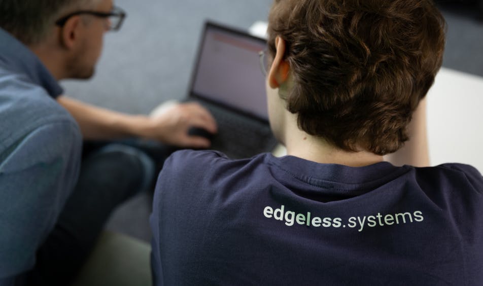 two men looking at a screen, from behind. One is wearing the Edgeless Systems branded tshirt