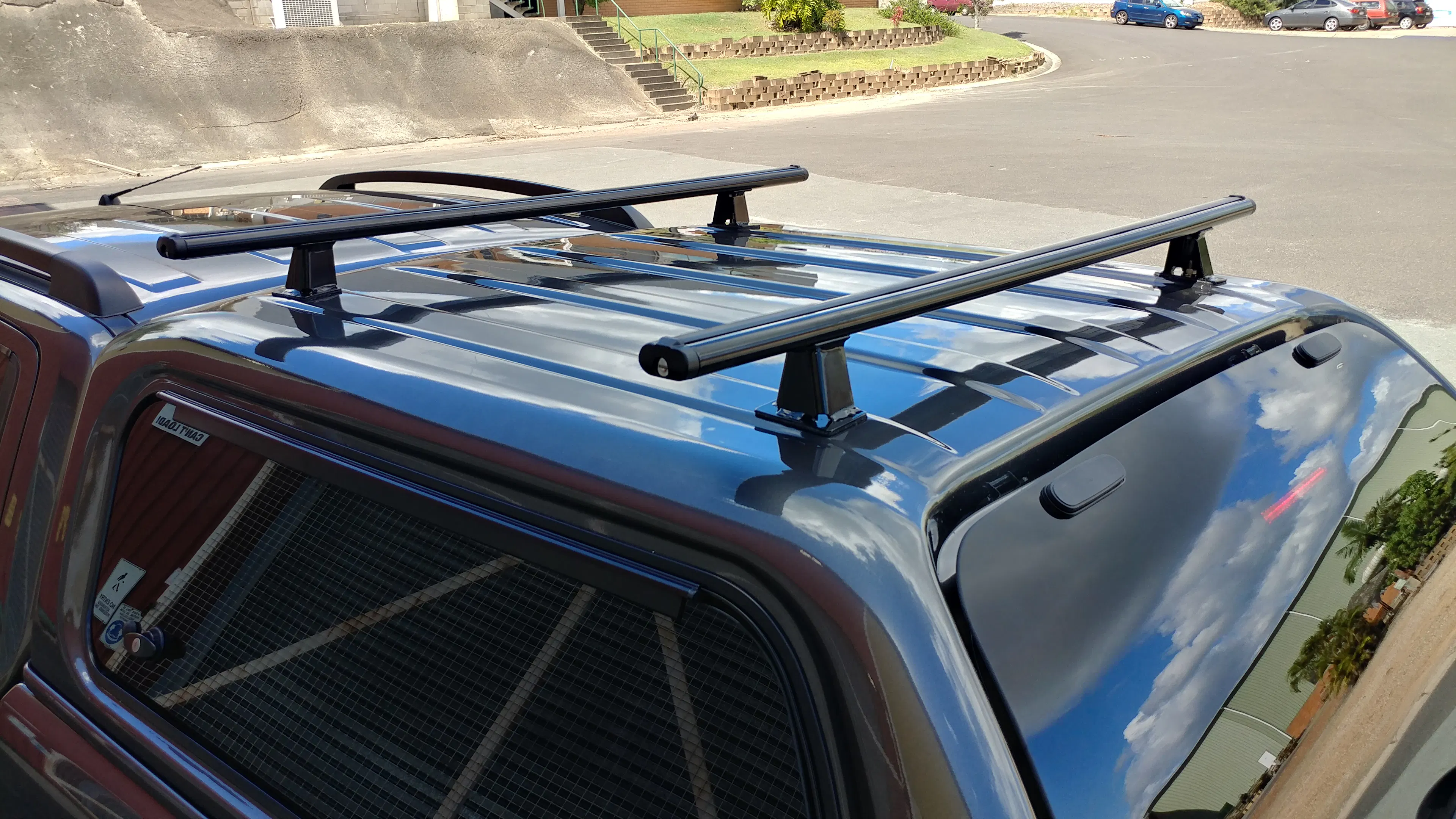 Black roof rack crossbars mounted on a blue ute canopy