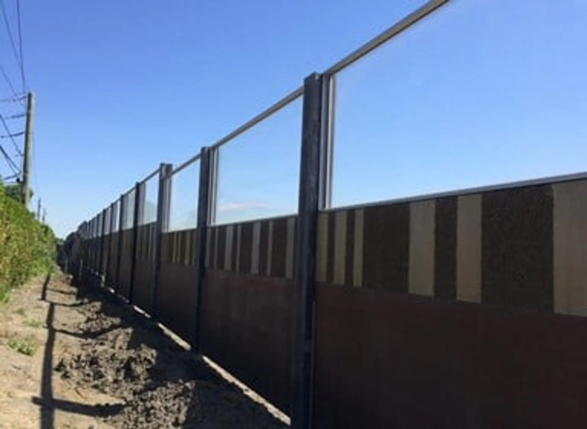 Brown noise wall topped with transparent panels running along the boulevard under a clear sky