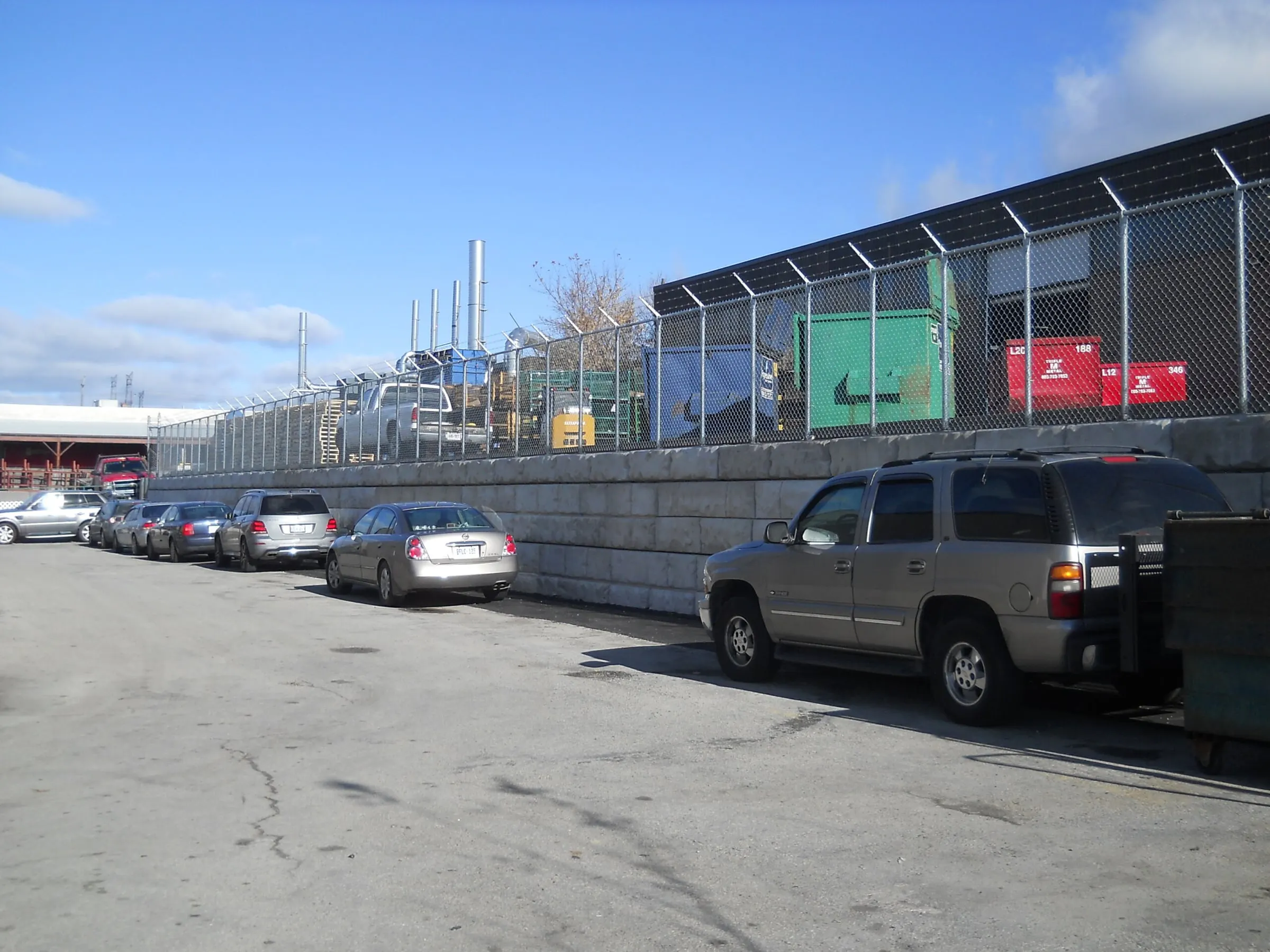 Completed precast retaining wall with security fencing above, holding back the neighbouring yard along the plant's parking lane