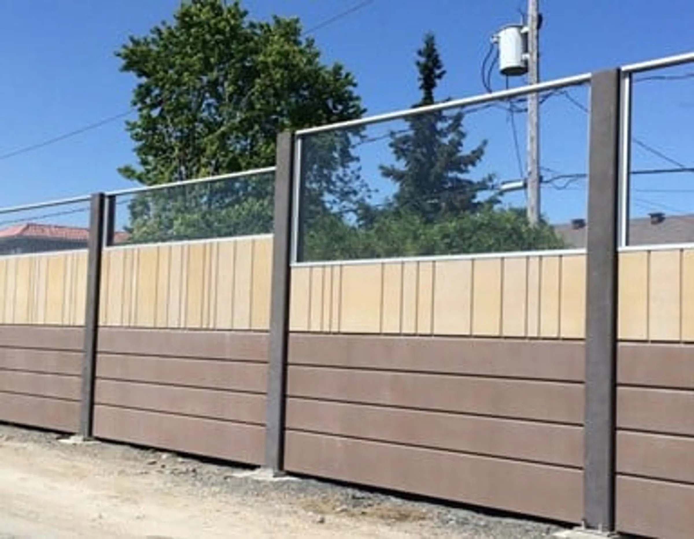 Two-tone noise wall with transparent Acrylite panels above a solid absorptive base, seen from the roadside