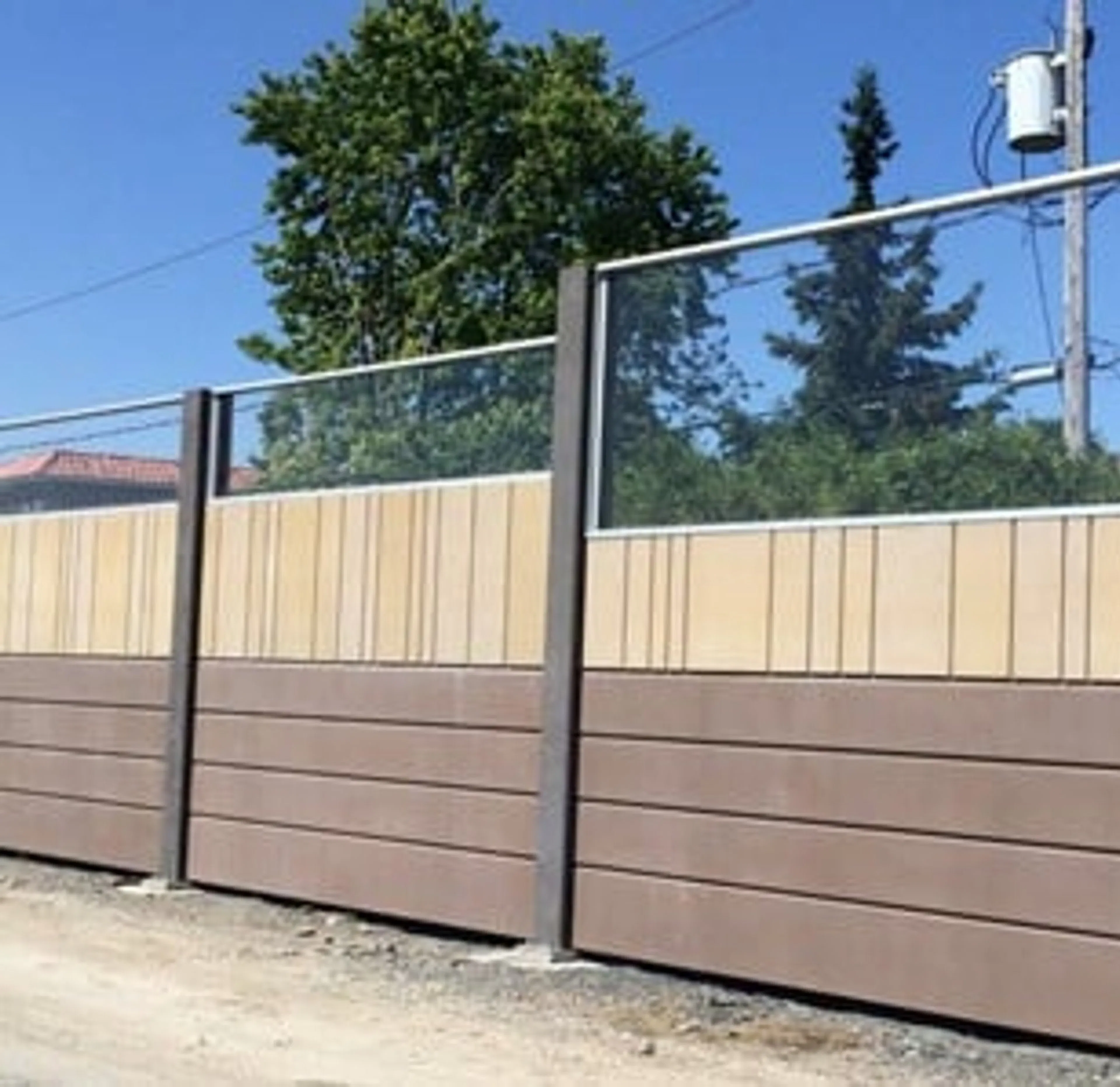 Two-tone noise wall with transparent panels above a solid absorptive base, seen from the roadside
