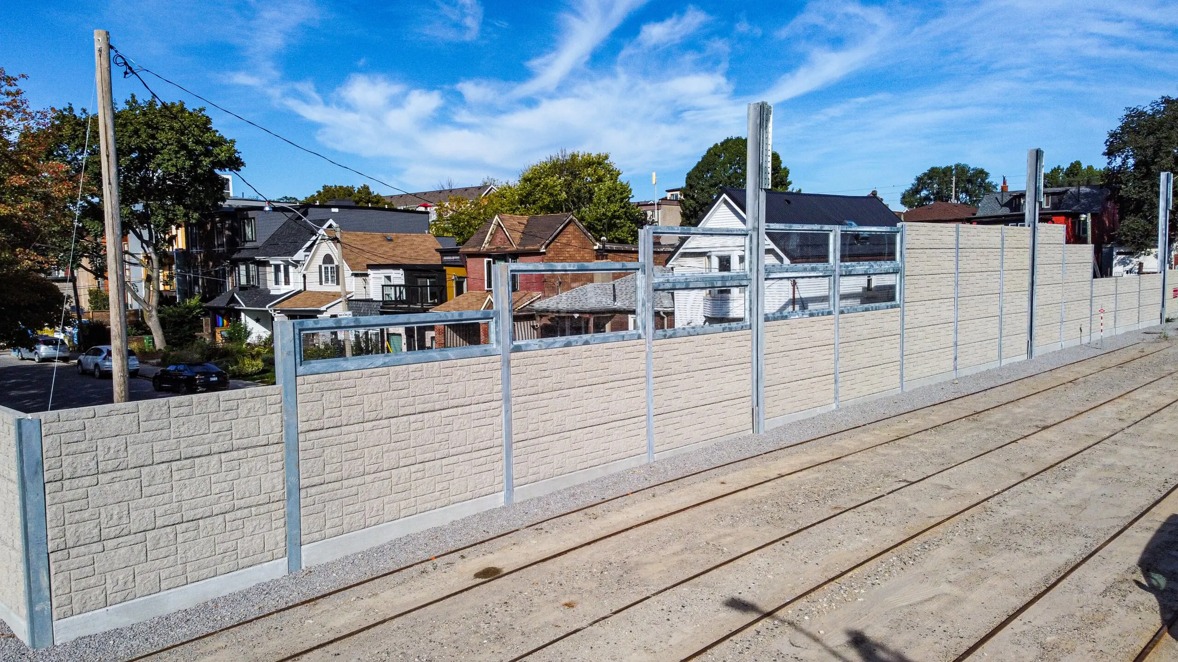 Acoustic wall with transparent upper panels alongside the streetcar tracks, neighbouring houses visible behind it
