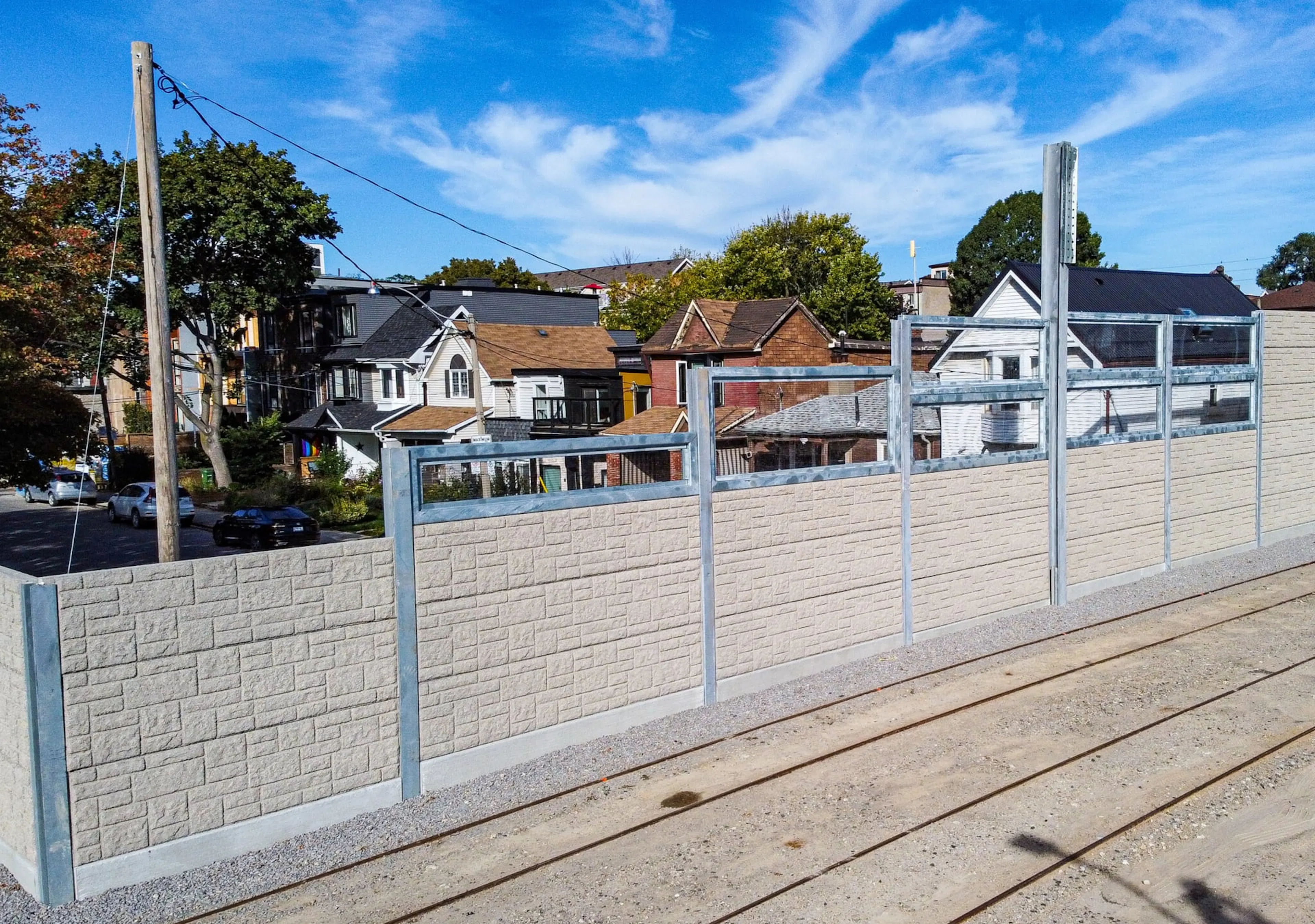 Acoustic wall with transparent upper panels alongside the streetcar tracks, neighbouring houses visible behind it