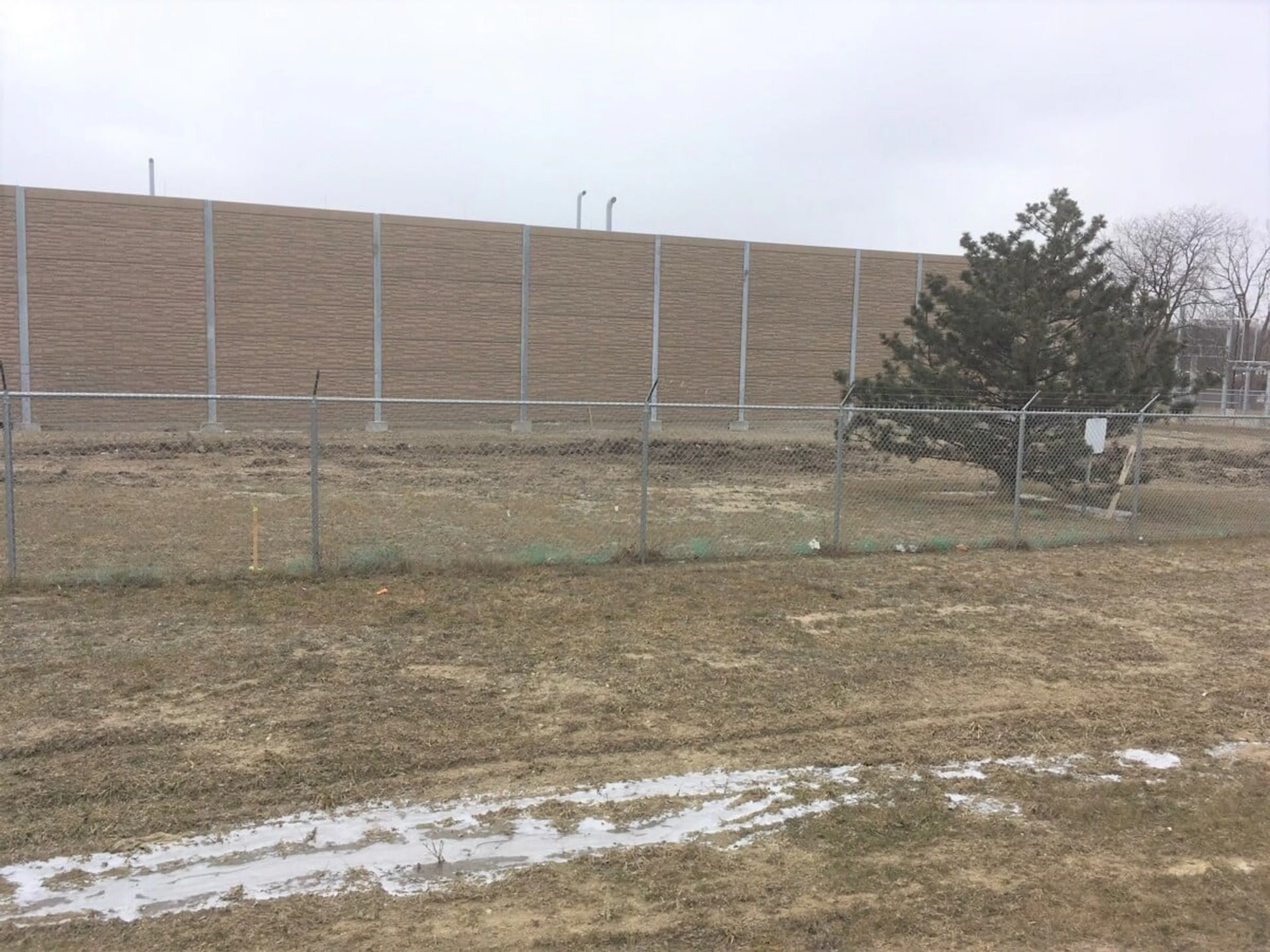 Noise wall seen across the field from the property line, screening the landfill gas equipment from neighbours
