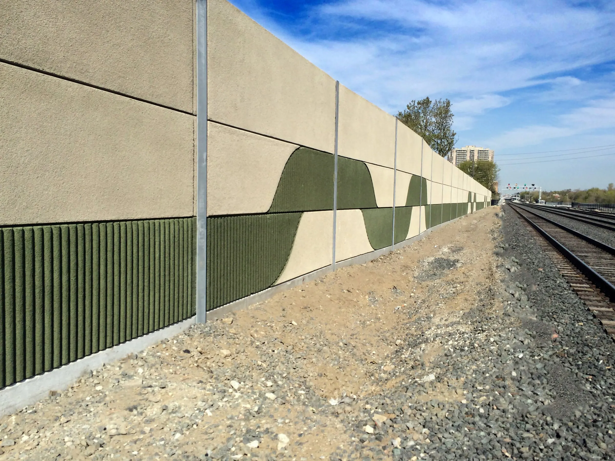 UP Express noise wall with a custom green wave pattern and ribbed panels beside the rail corridor