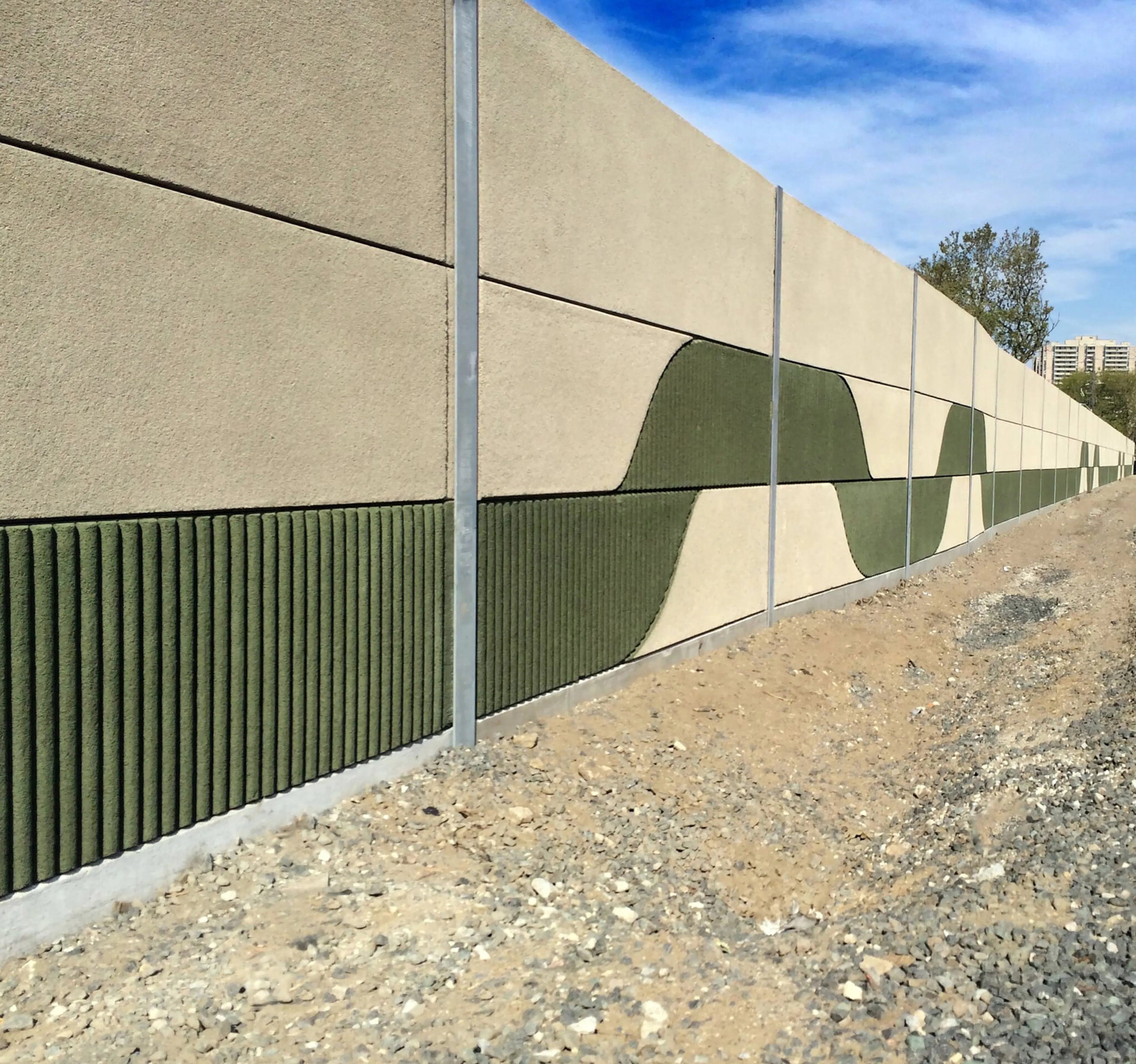 UP Express noise wall with a custom green wave pattern and ribbed panels beside the rail corridor