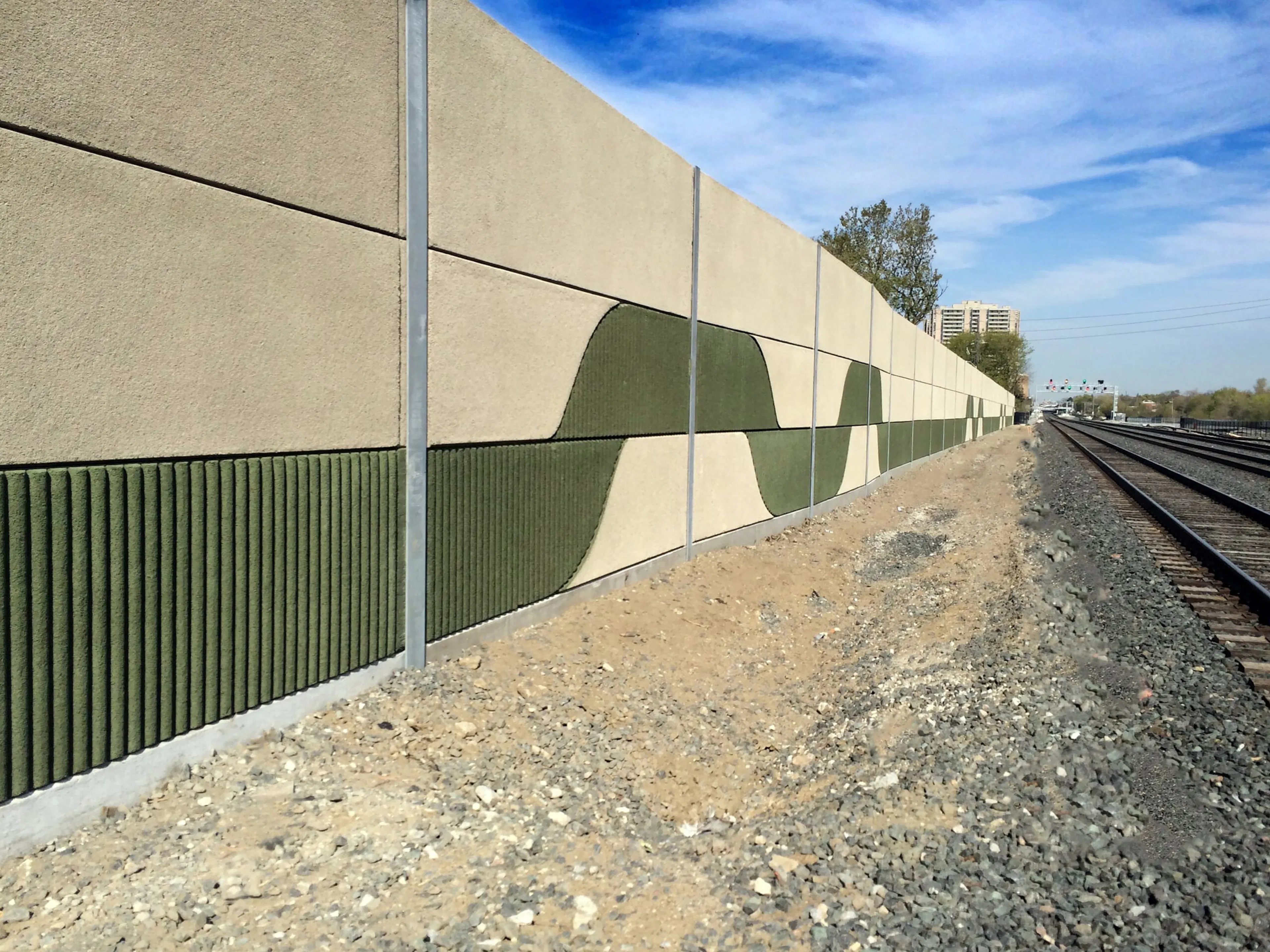 UP Express noise wall with a custom green wave pattern and ribbed panels beside the rail corridor
